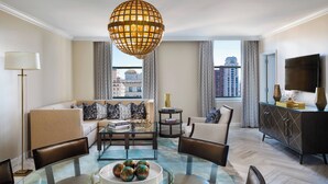 A modern living room with a glass coffee table, leather chairs, a sofa with patterned cushions, a hanging spherical light fixture, and a view of the city through large windows. - The Ritz-Carlton, Philadelphia (Philadelphia)