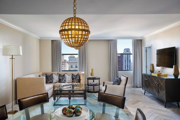 A modern living room with a glass coffee table, leather chairs, a sofa with patterned cushions, a hanging spherical light fixture, and a view of the city through large windows. - The Ritz-Carlton, Philadelphia (Philadelphia)