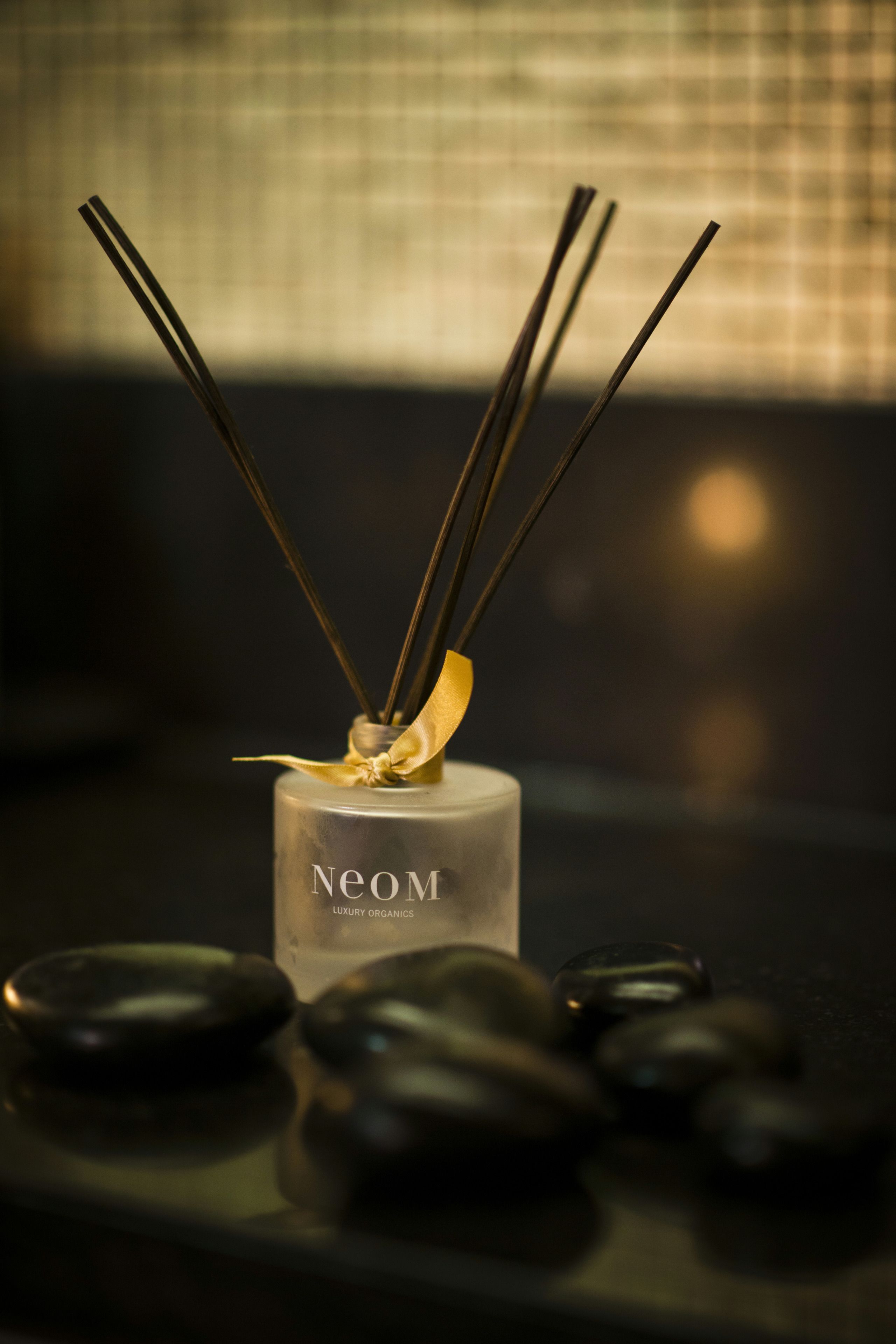 A bottle of Neom Luxury Organics with reed diffusers and black stones on a tray.