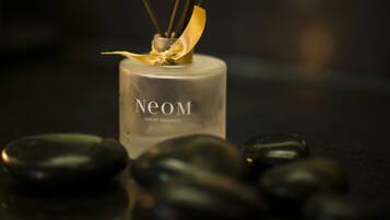 A bottle of Neom Luxury Organics with reed diffusers and black stones on a tray.