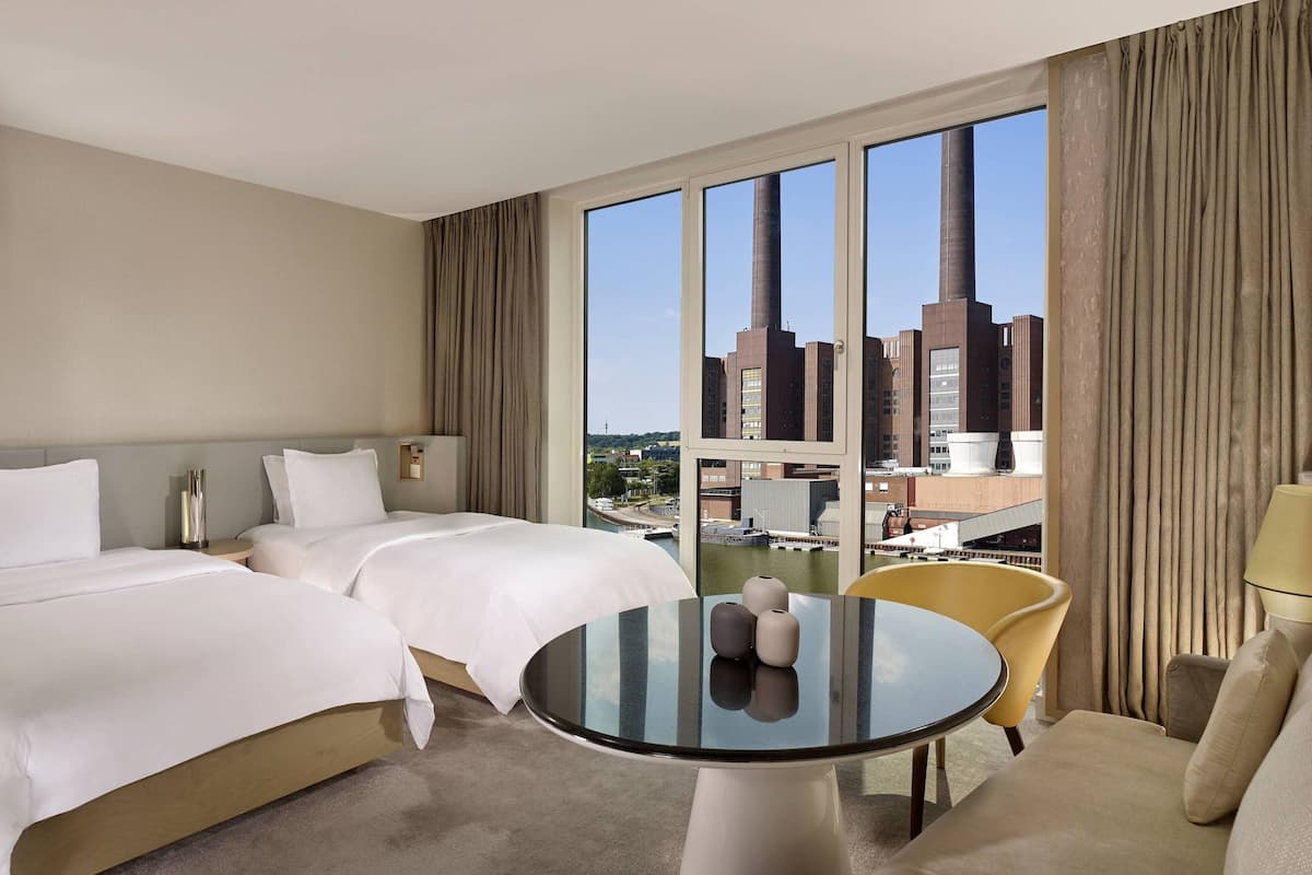Ein Hotelzimmer mit zwei Betten, einem runden Tisch und Blick auf eine Stadtansicht.