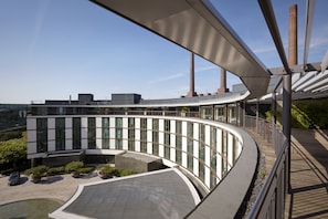 A modern building with a curved glass facade, large windows, and a rooftop terrace.
