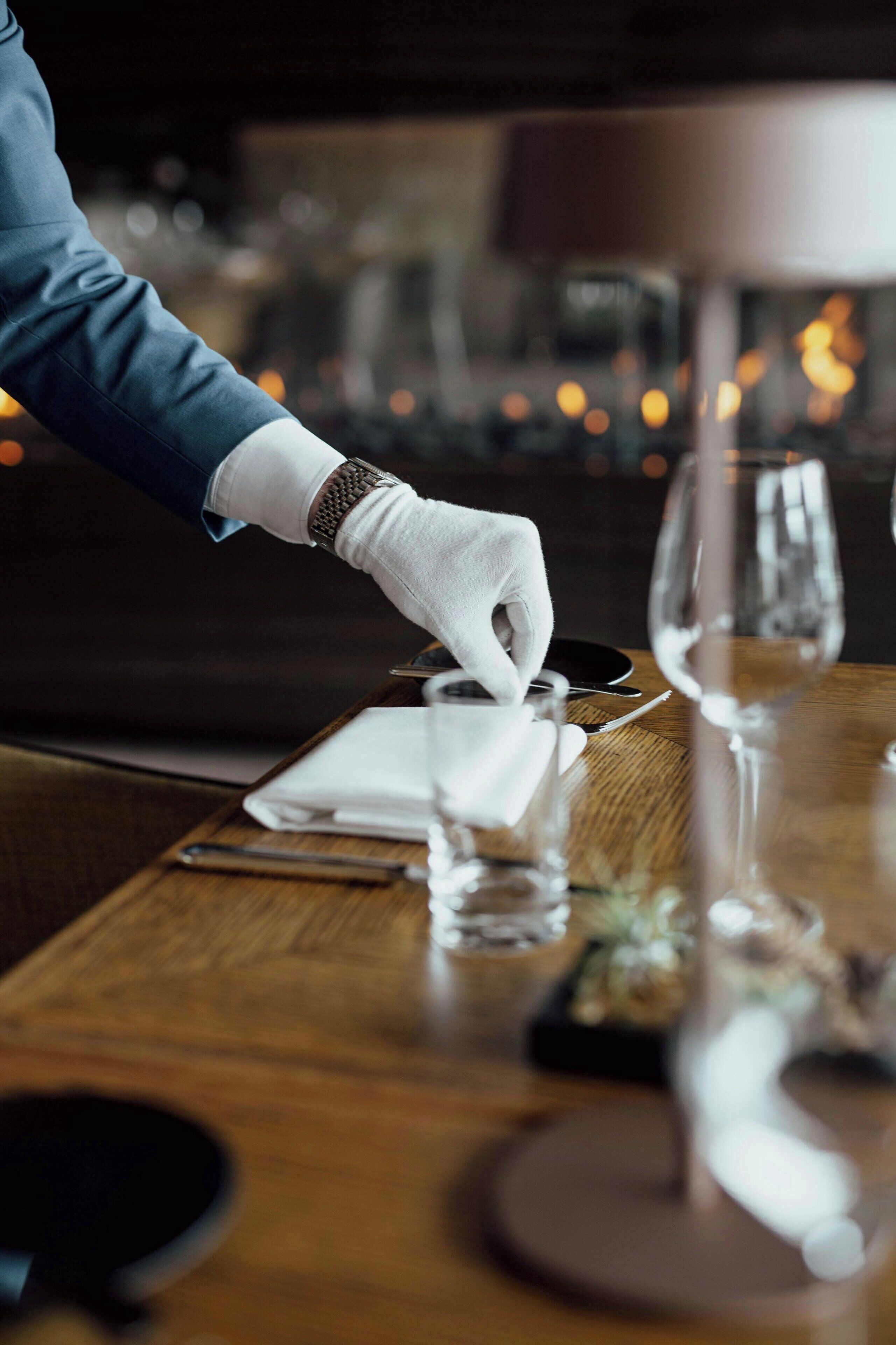 A person setting a table with a white napkin and a wine glass.