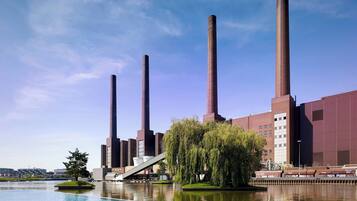 Een groot industriële complex met hoge schoorstenen en een rustig waterlichaam op de voorgrond.