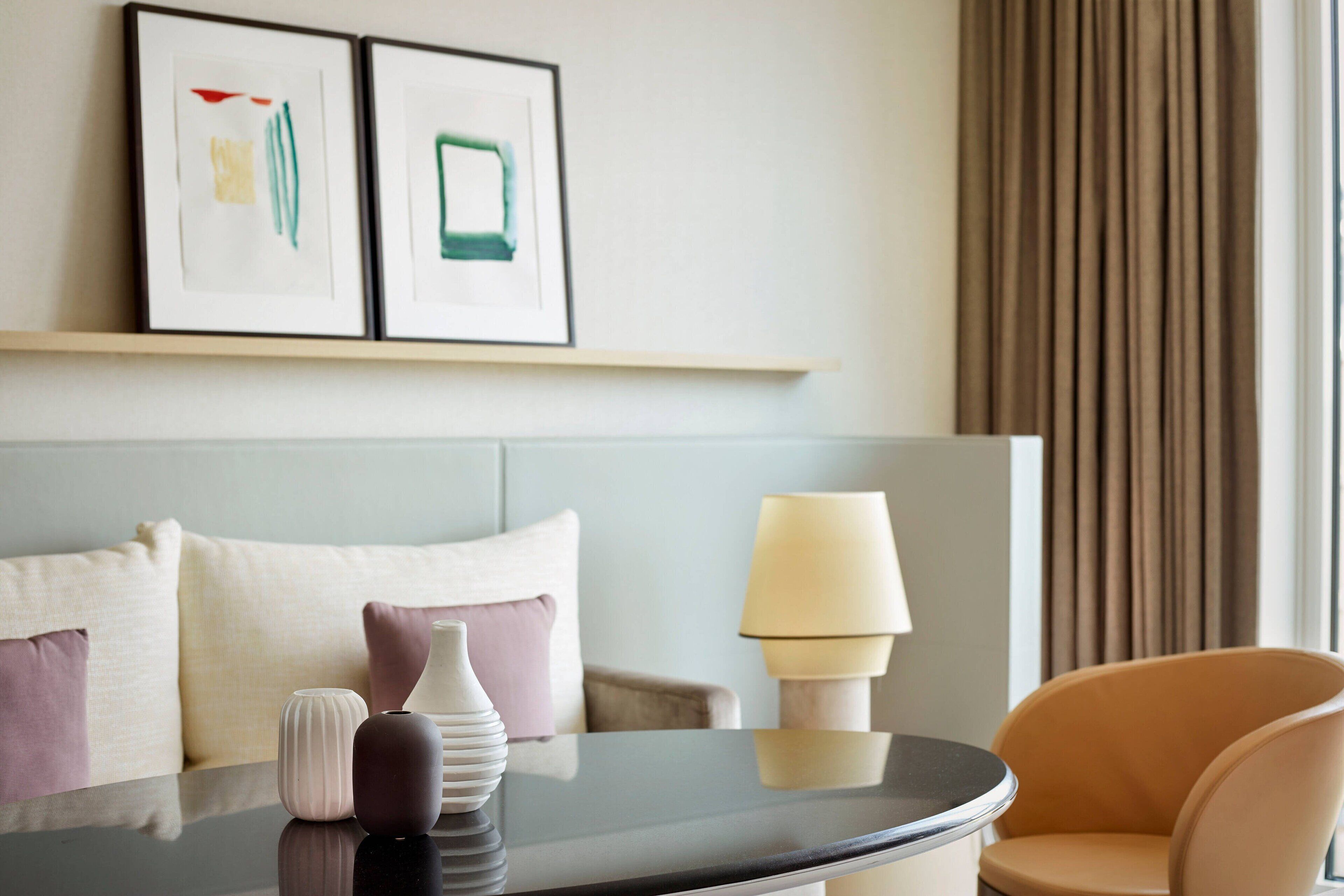 A hotel room with a bed, a table with decorative items, a lamp, and a chair.
