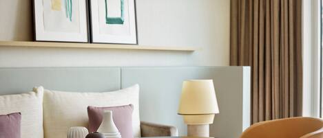 A hotel room with a bed, a table with decorative items, a lamp, and a chair.