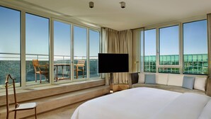 A hotel room with a large bed, a TV, a balcony with chairs, and a view of the city. - The Ritz-Carlton, Wolfsburg (Wolfsburg)