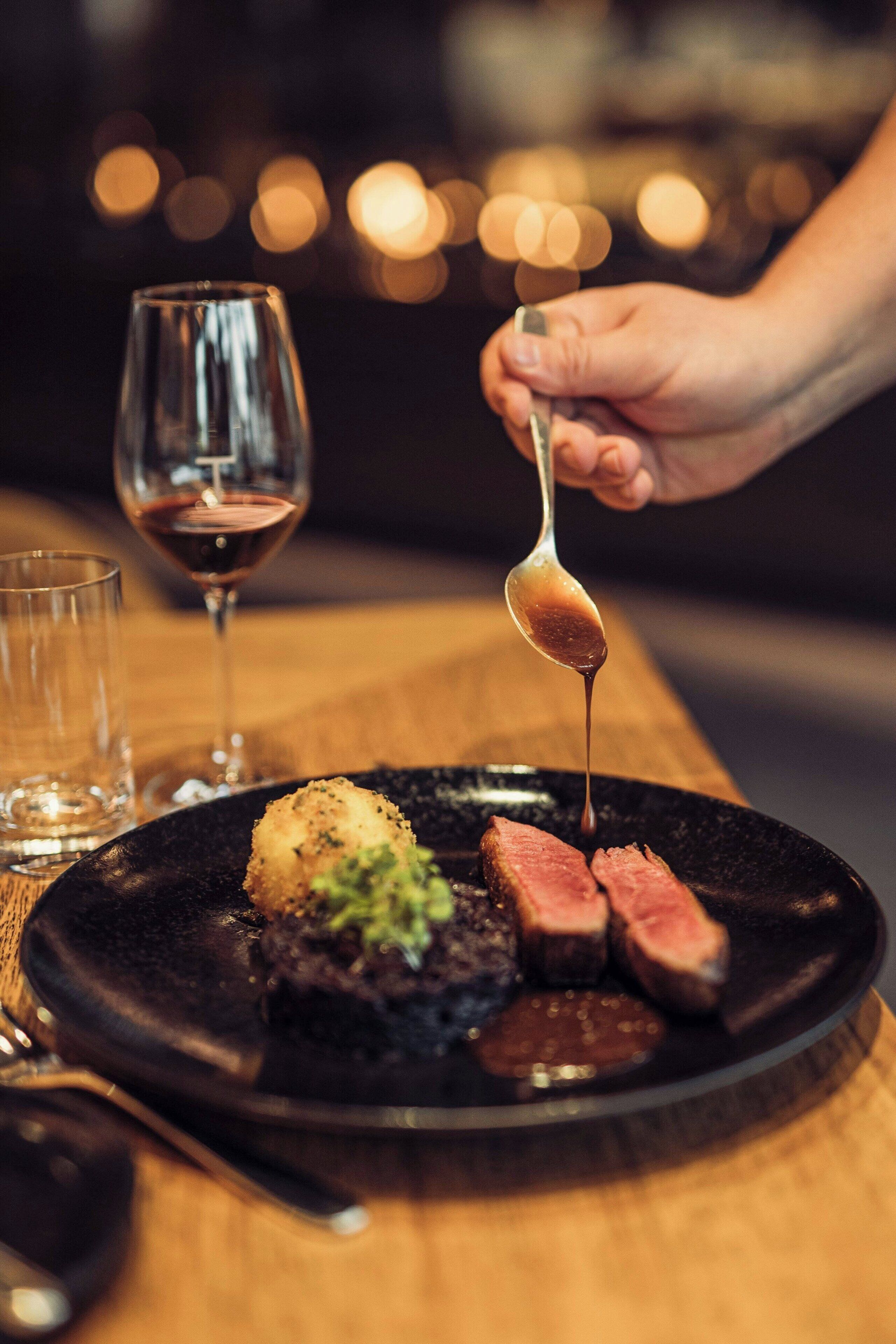 Un piatto con bistecca e salsa, un bicchiere di vino rosso e un cucchiaio.