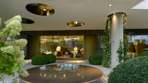 A modern building with a circular water feature, a glass entrance, and a well-maintained garden. - The Ritz-Carlton, Wolfsburg (Wolfsburg)