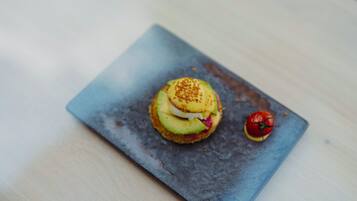 A square plate with a sandwich and a tomato on a wooden table.