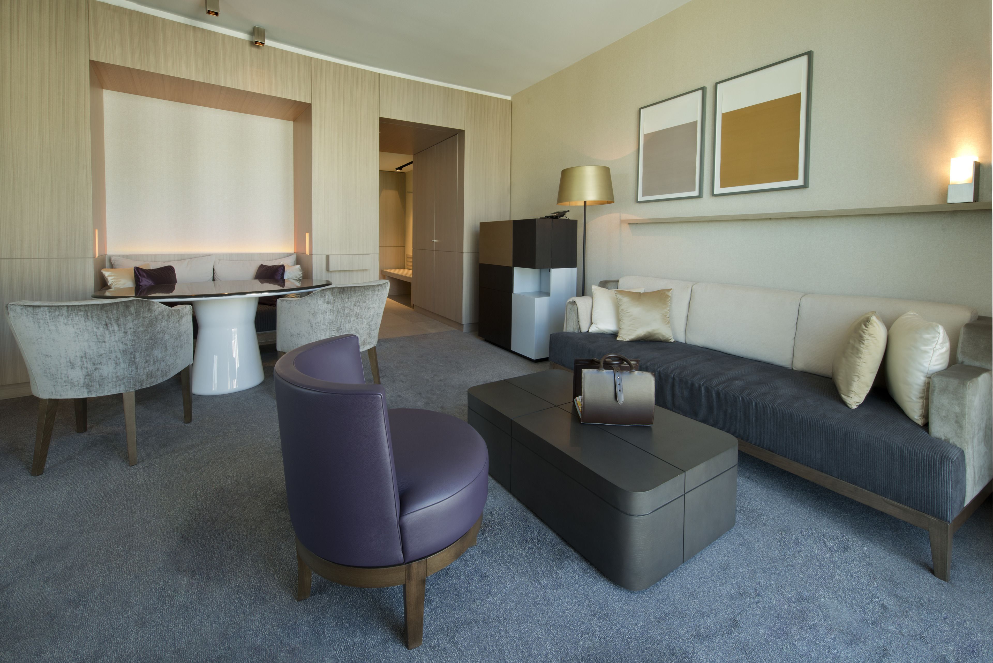 A modern hotel room with a sofa, a coffee table, a chair, and a desk area.