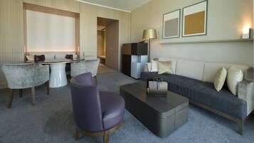 A modern hotel room with a sofa, a coffee table, a chair, and a desk area.