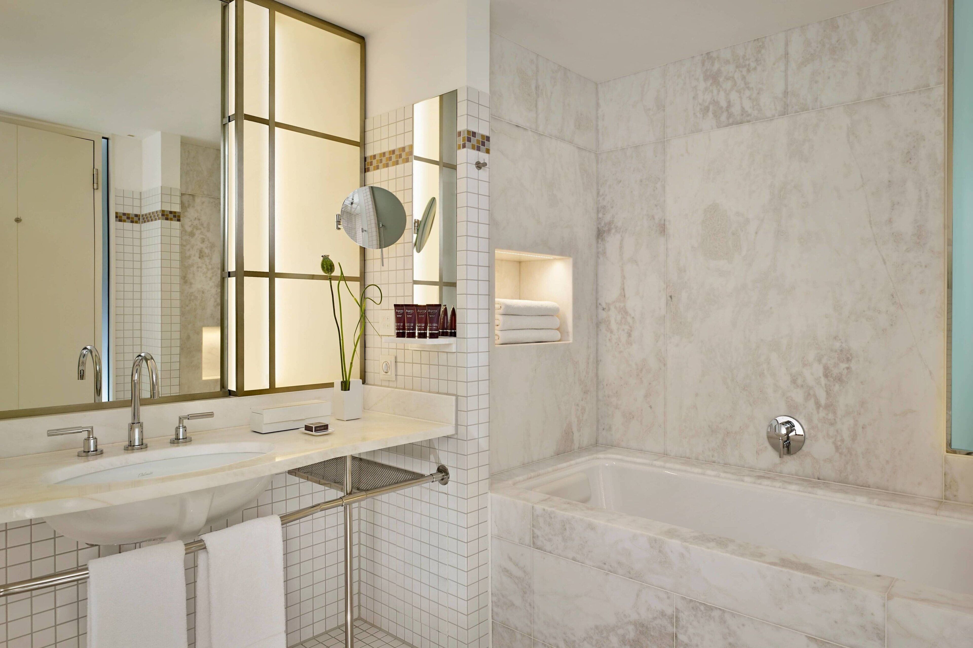 A modern bathroom with a large mirror, a double sink, and a bathtub.
