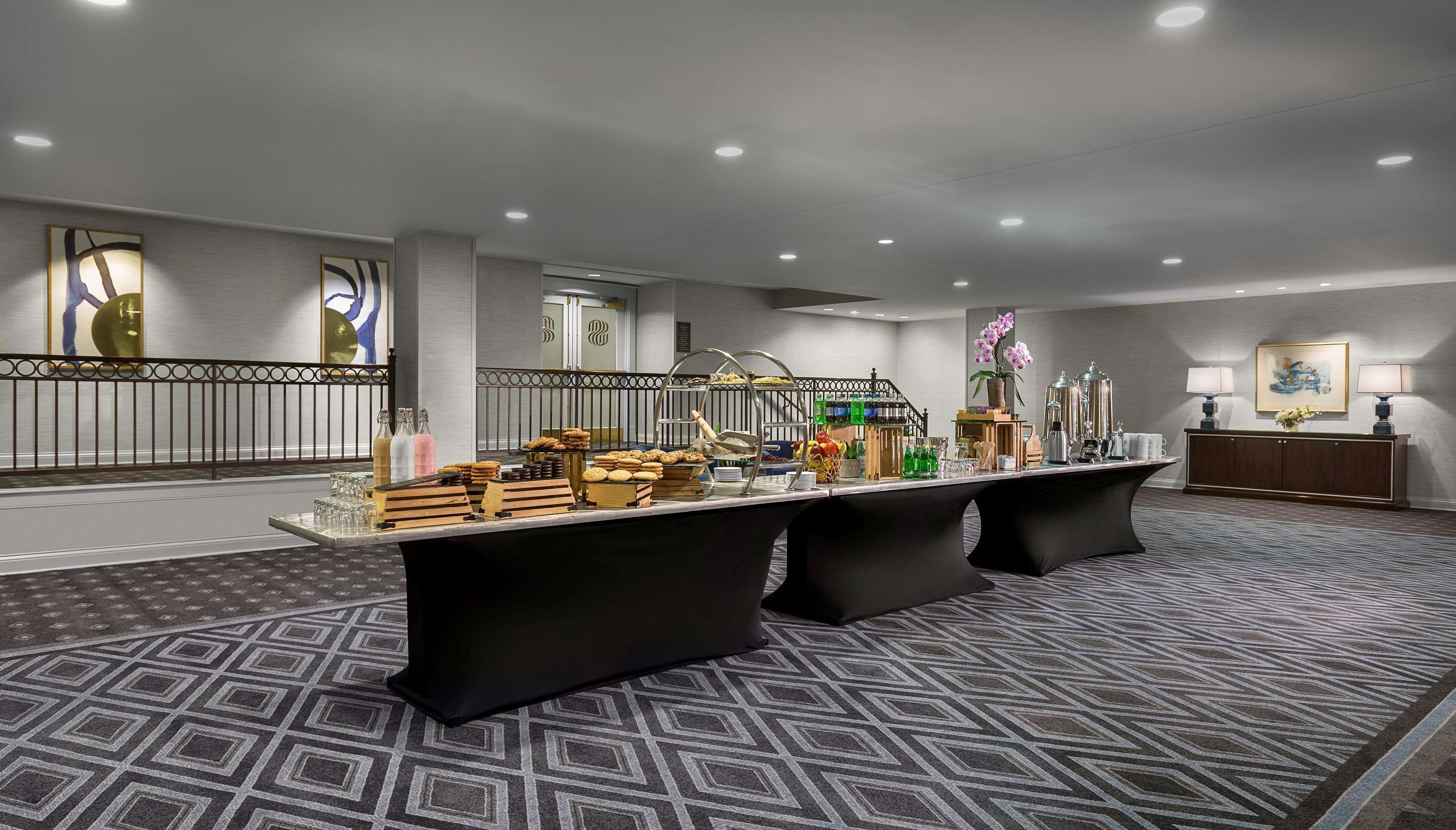 A spacious hotel lobby with a long reception desk, a decorative railing, and a patterned carpet.