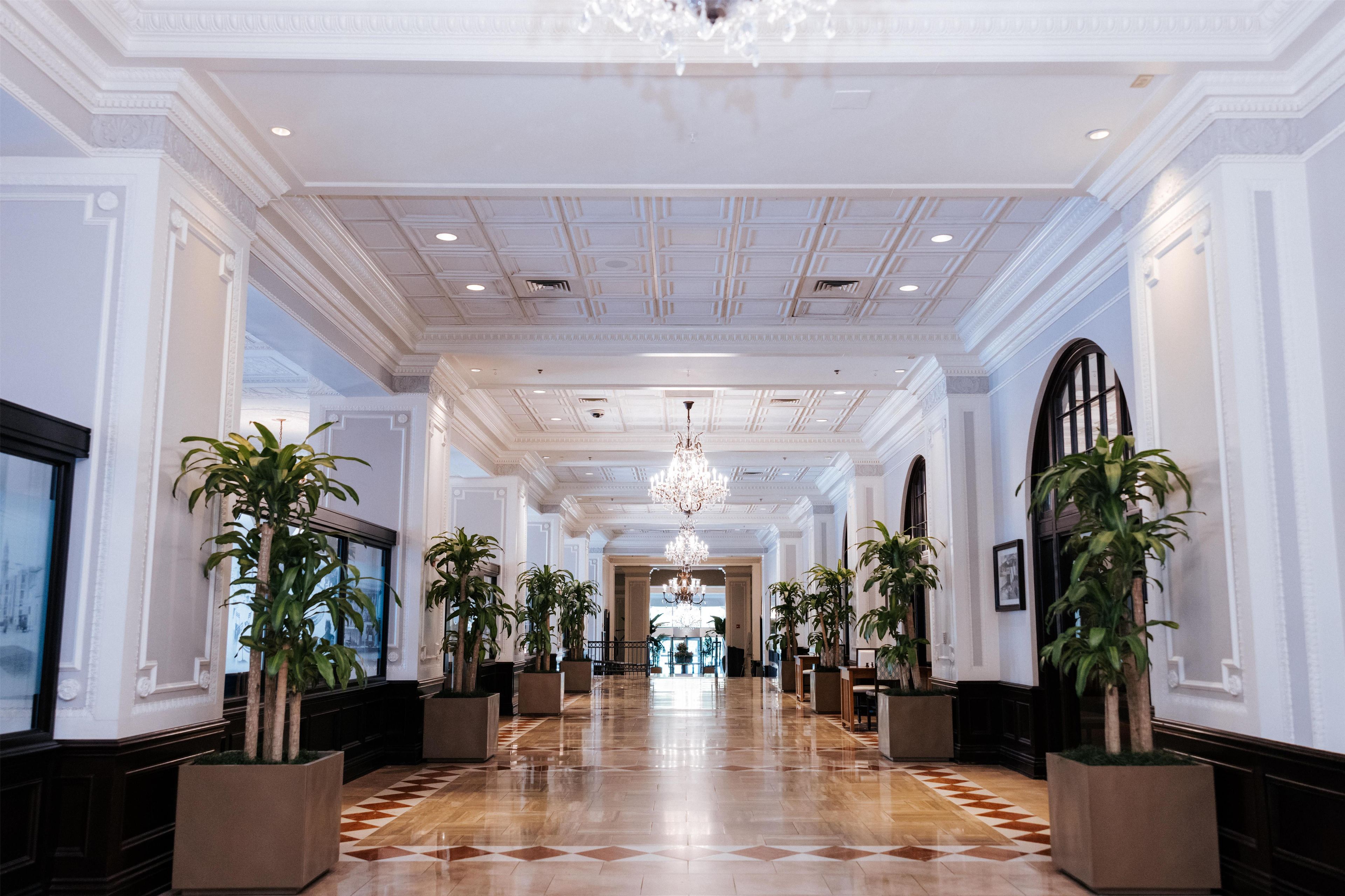 Un vestíbulo de hotel con un largo pasillo, grandes candelabros y plantas en macetas.