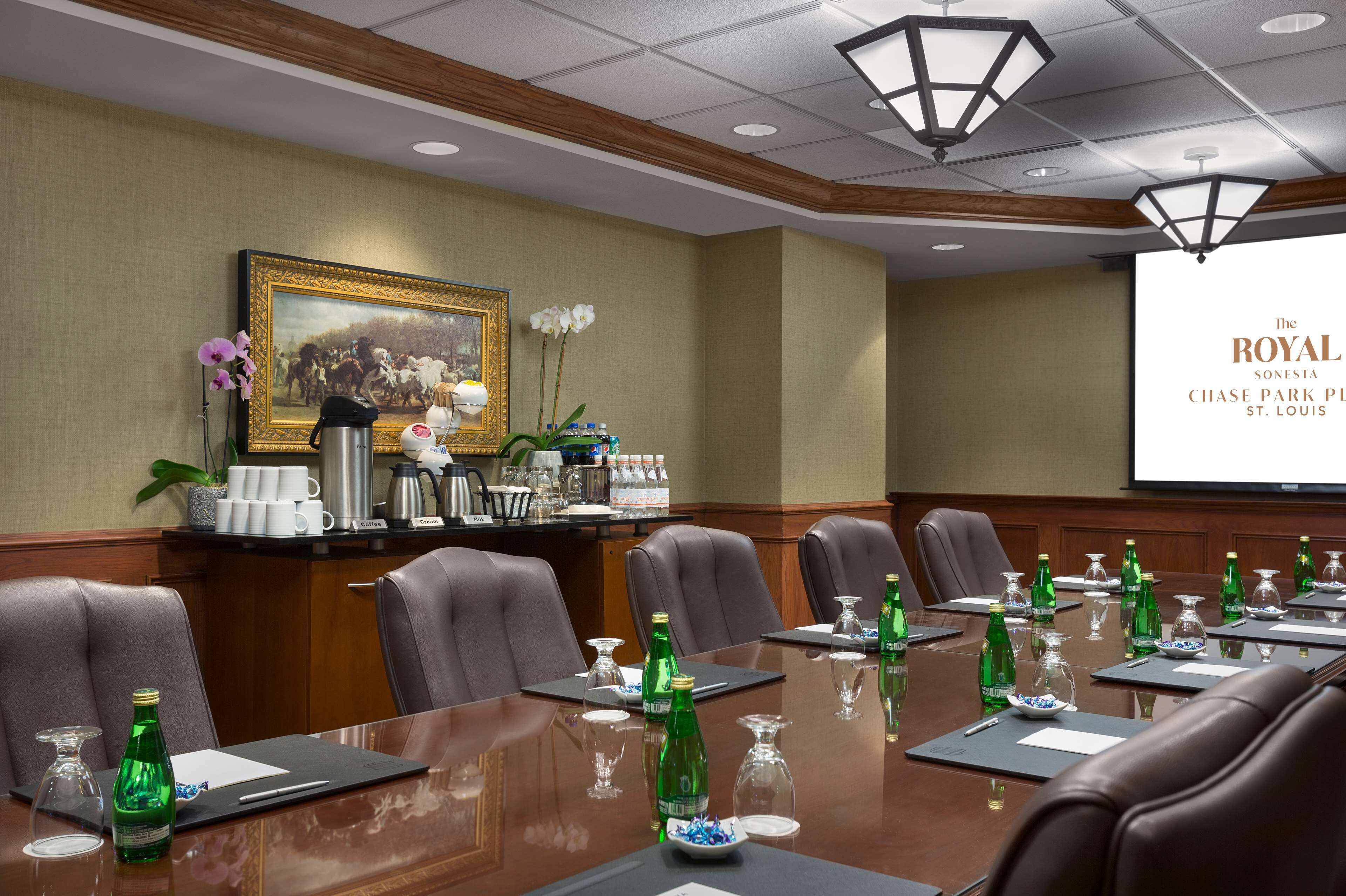 A conference room with a long table, multiple chairs, and a projector screen displaying "The Royal Sonesta Chase Park Place St. Louis".