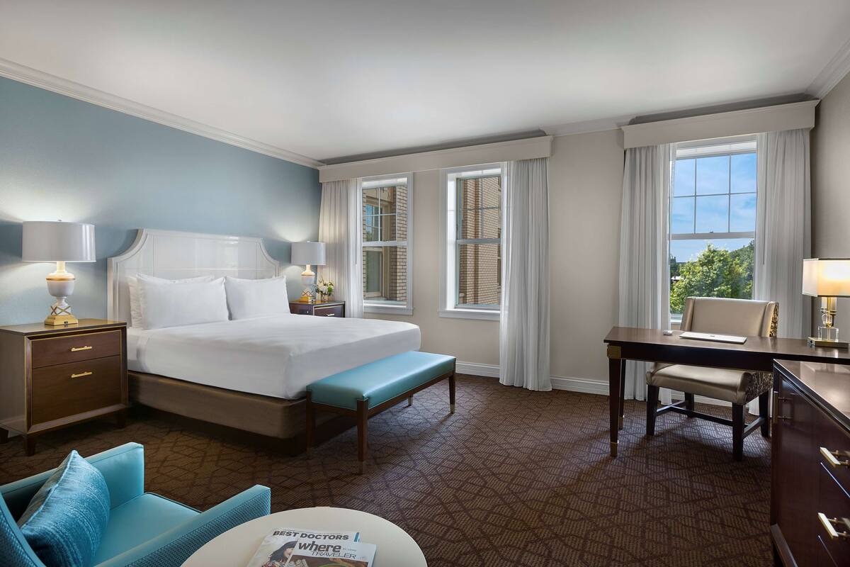 Une chambre d’hôtel avec un grand lit, des tables de chevet avec des lampes, un bureau et une chaise.