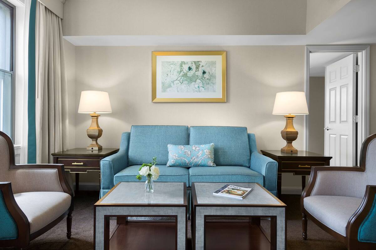 Une chambre d’hôtel avec un canapé bleu, deux fauteuils, une table basse et un tableau au mur.