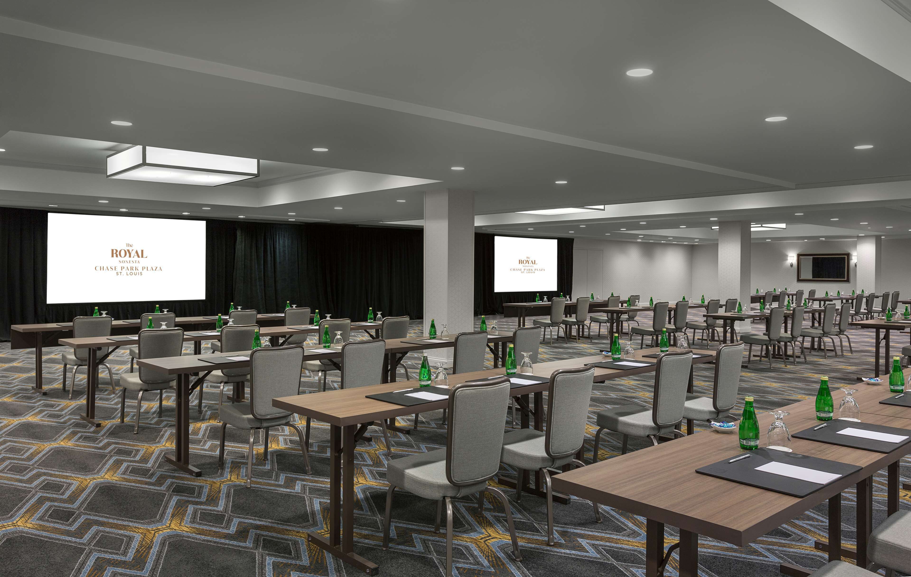 Une salle de conférence d’hôtel équipée de plusieurs tables, de chaises et d’un grand écran affichant le nom de l’hôtel.