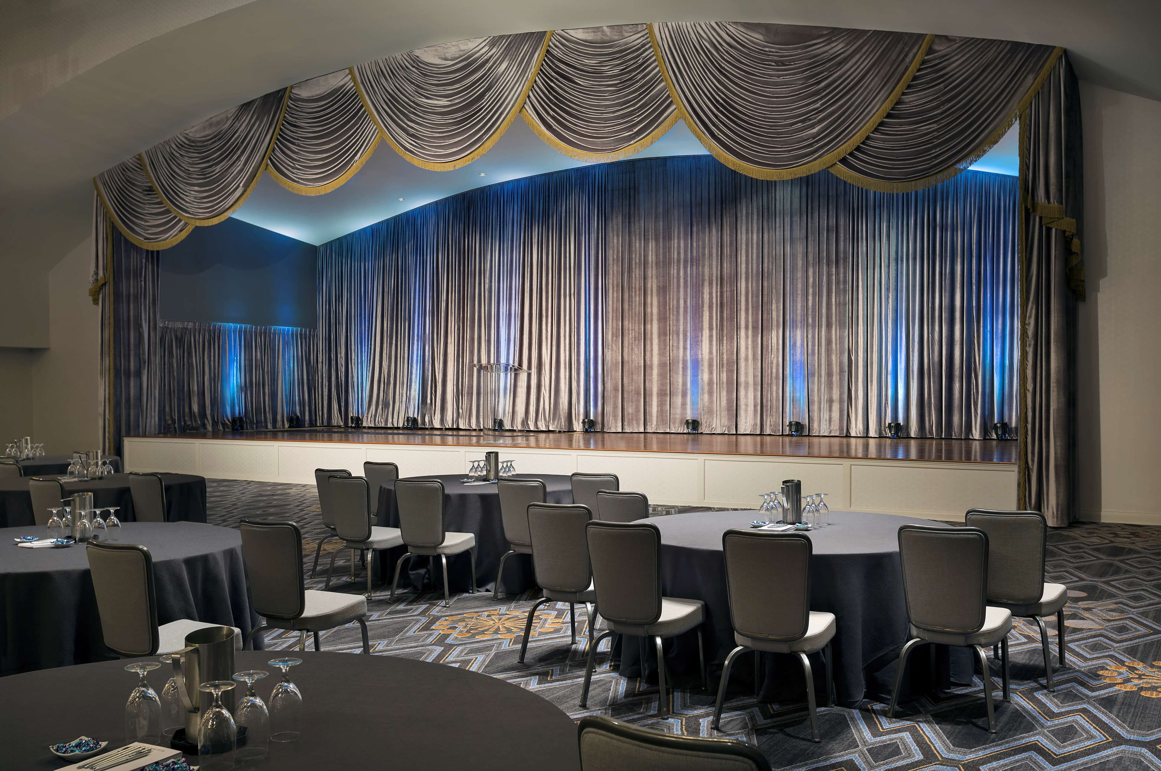 A conference room with round tables, chairs, and a large curtain backdrop.