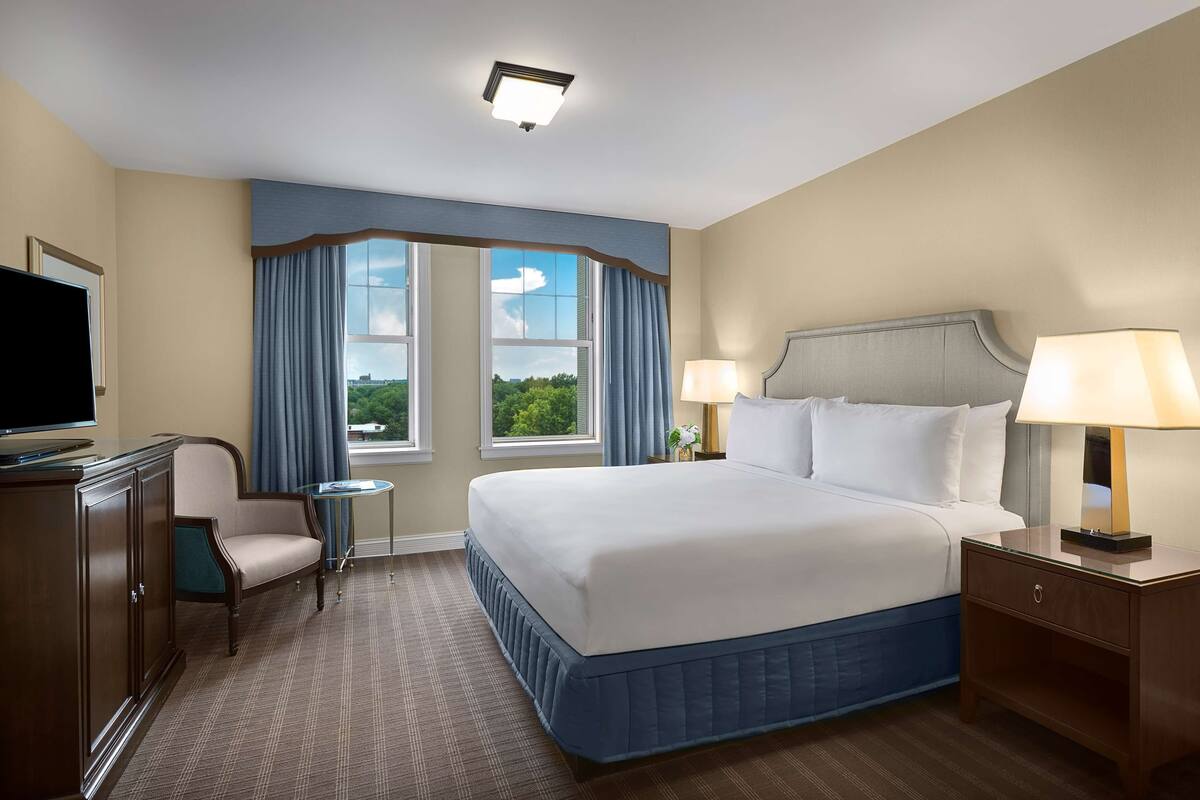 Une chambre d’hôtel avec un grand lit, deux lampes de chevet, une télévision, un bureau avec une chaise et une vue sur l’extérieur par une fenêtre.