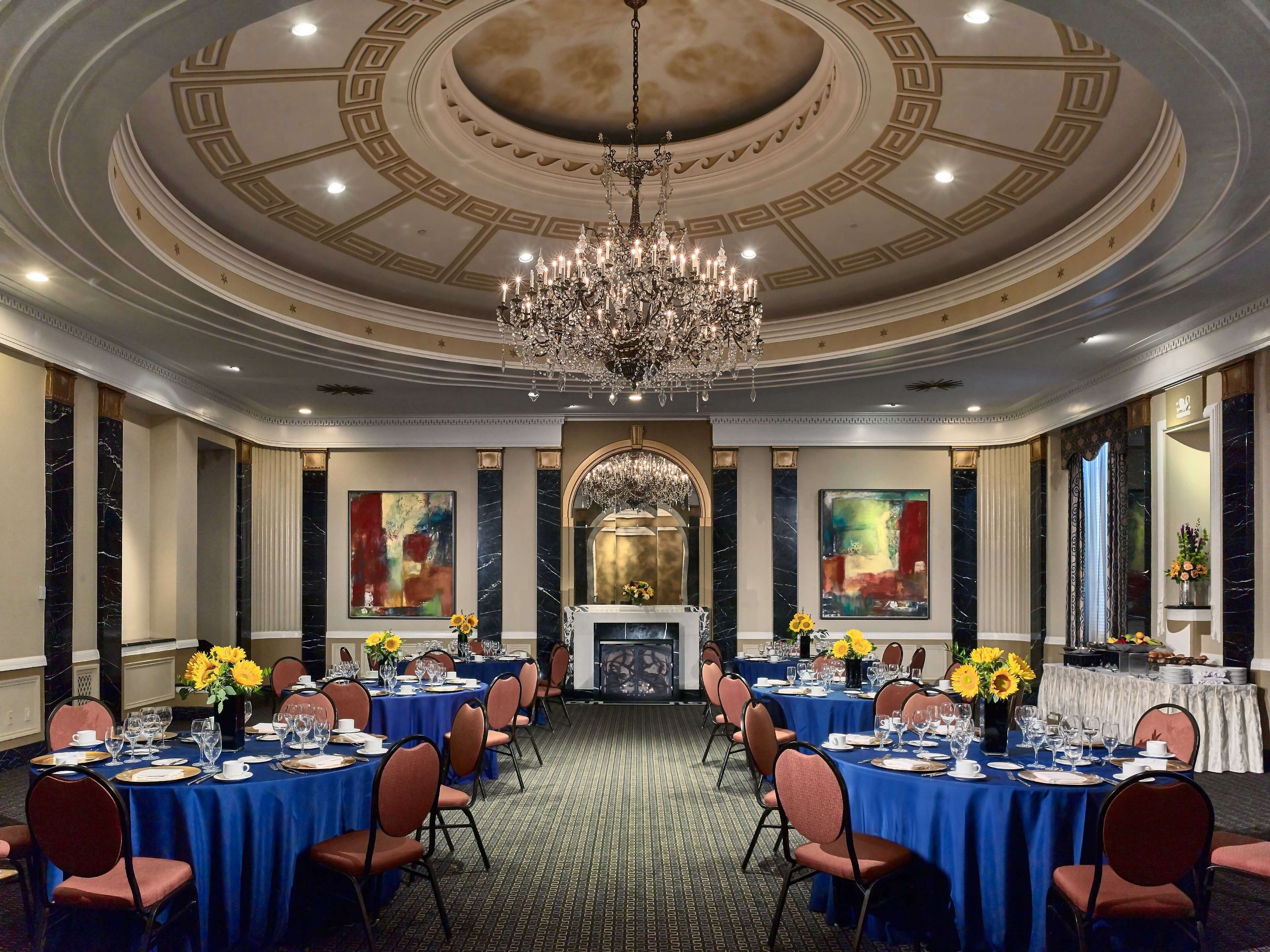 A formal dining room with round tables, blue tablecloths, and red chairs.