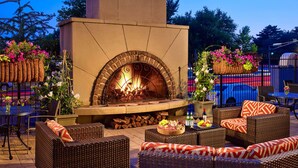 An outdoor patio with a brick fireplace, wicker furniture, and a dining table set with food and drinks. -  The Royal Sonesta Chase Park Plaza St. Louis (St. Louis)