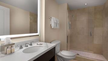 A modern bathroom with a large mirror, two sinks, a toilet, and a walk-in shower.