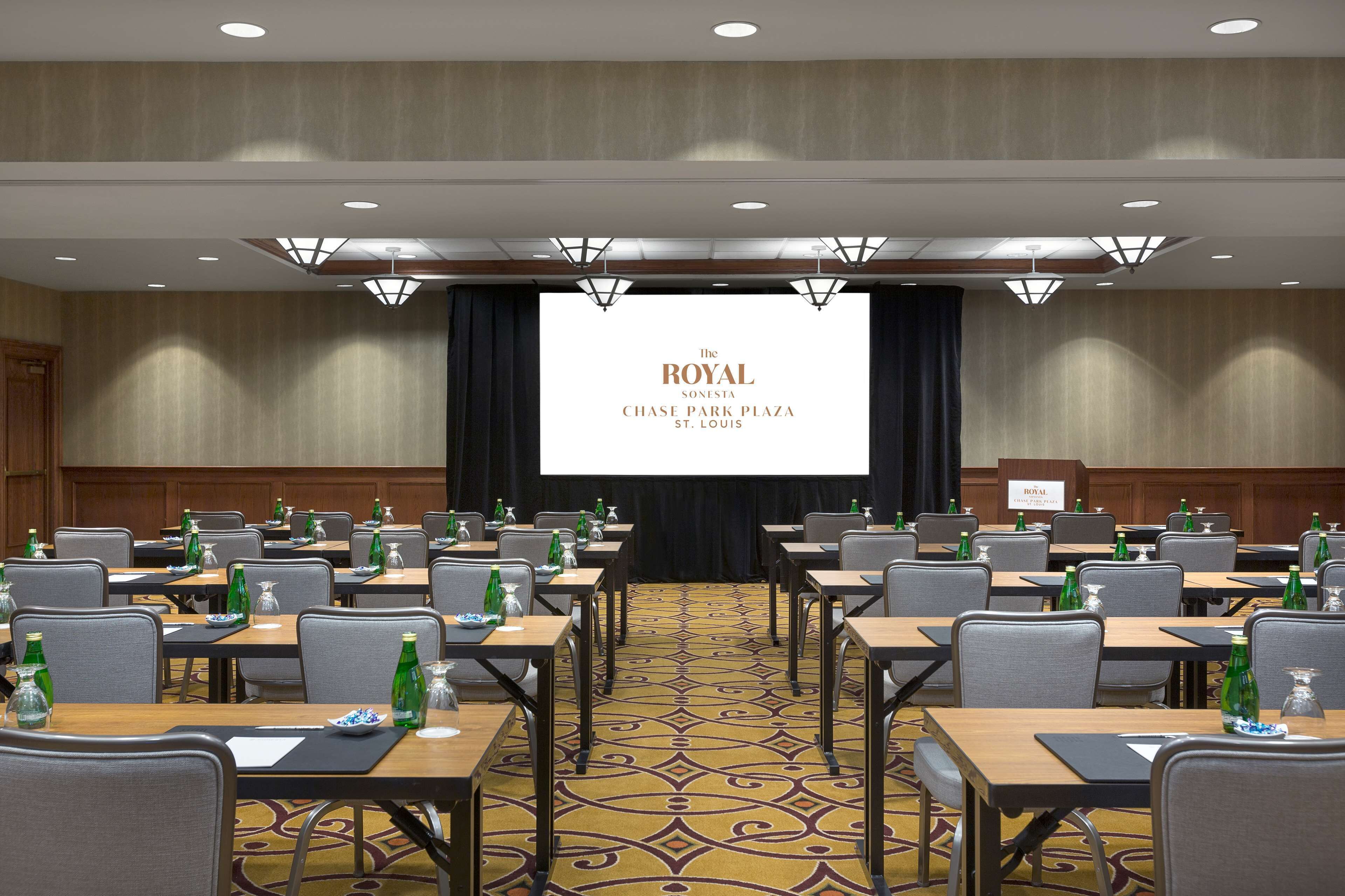 A conference room with multiple tables, chairs, and a large screen displaying "The Royal Sonsesta Chase Park Plaza St. Louis".