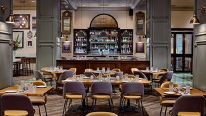 A restaurant with multiple dining tables and chairs, a bar area with shelves of bottles, and a large mirror above the bar. -  The Royal Sonesta Chase Park Plaza St. Louis (St. Louis)