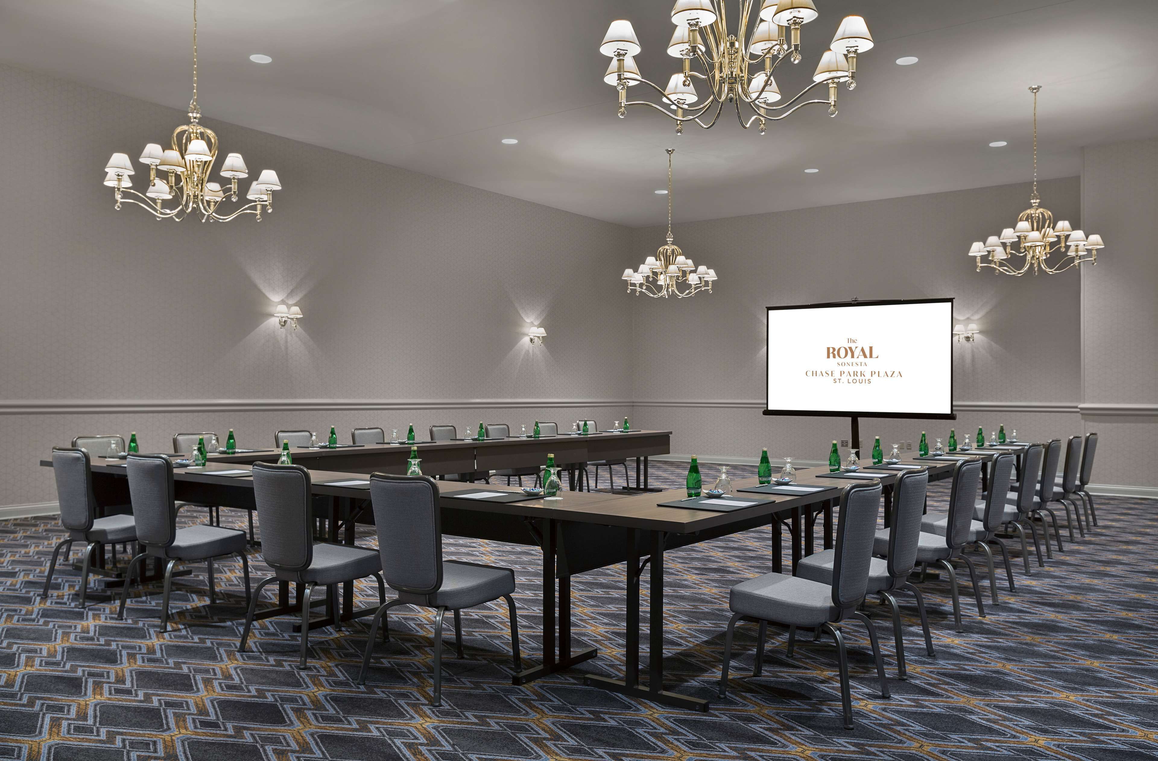 A conference room with a long table, multiple chairs, and chandeliers. A projector screen displays "The Royal Chatea" on the wall.