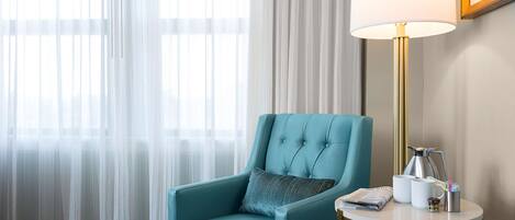 A teal armchair with a cushion, a small round table with a lamp, a coffee pot, and a mug.