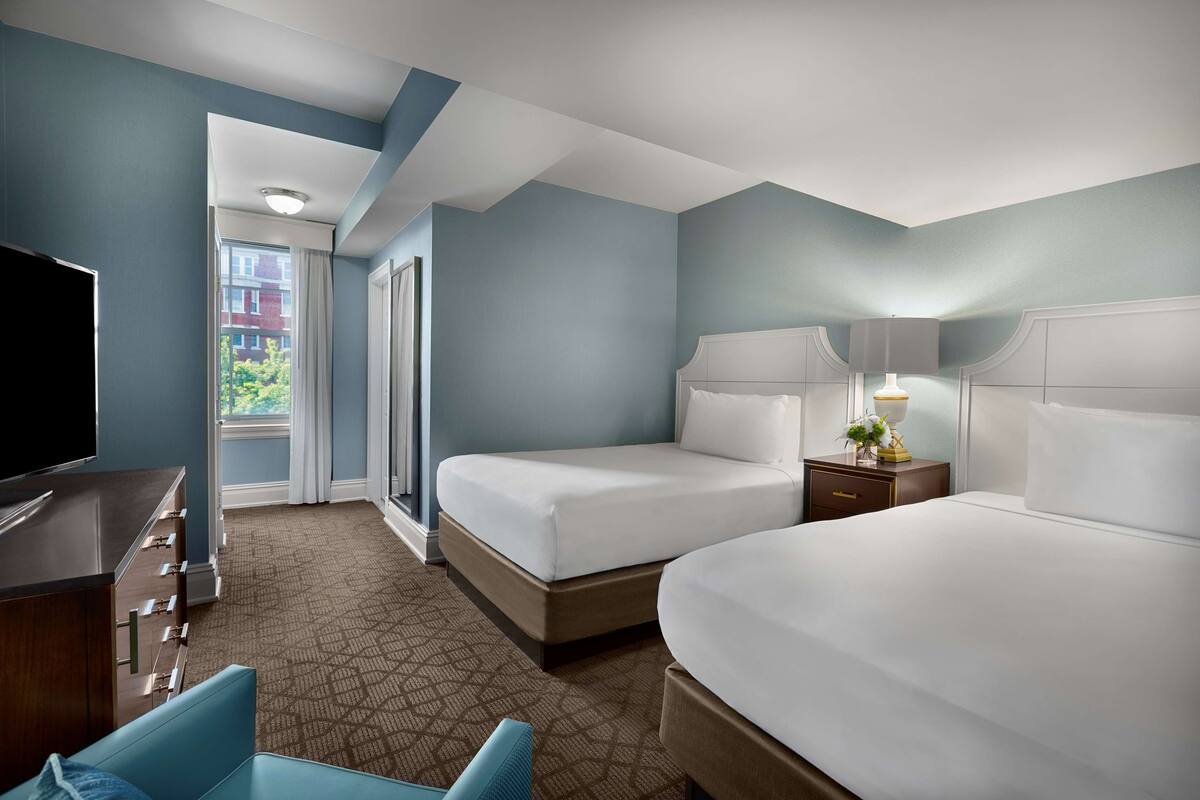 Une chambre d’hôtel avec deux lits, une télévision, un bureau et une vue sur l’extérieur.