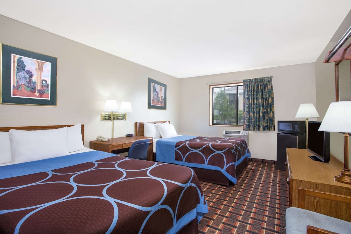 Habitación de hotel con dos camas, un escritorio, televisor y ventana con cortinas.