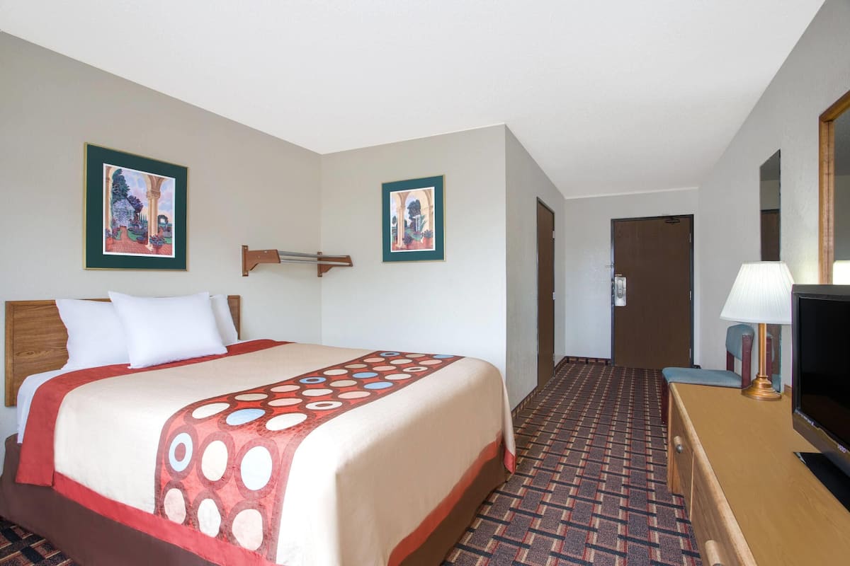 Habitación de hotel con cama, televisor, escritorio y dos cuadros en la pared.