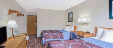 A hotel room with two beds, a desk with a lamp, a TV, and a patterned carpet.