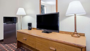Habitación de hotel con tocador de madera, televisor de pantalla plana, cafetera, microondas y dos lámparas.