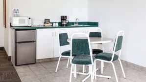 A compact kitchen with a refrigerator, microwave, coffee maker, and a sink. There are four chairs with green upholstery around a small round table. - Super 8 by Wyndham Morden (Morden)