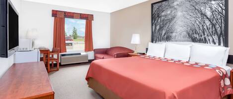 A hotel room with a large bed, a desk, a chair, a window with curtains, and a painting on the wall.