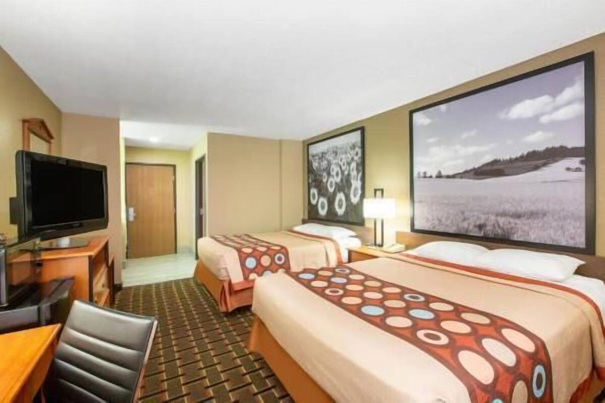 A hotel room with two beds, a TV, a desk, and a view of a snowy landscape.