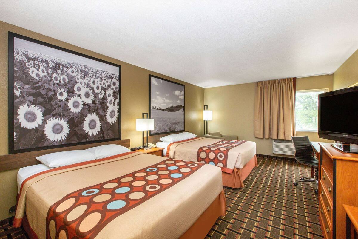 A hotel room with two beds, a TV, and a large floral painting on the wall.