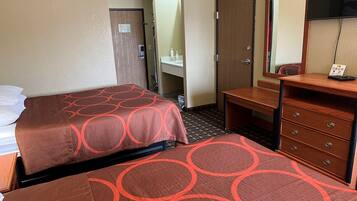 A hotel room with two beds, a wooden dresser, a mirror, and a bathroom with a sink and towel rack.