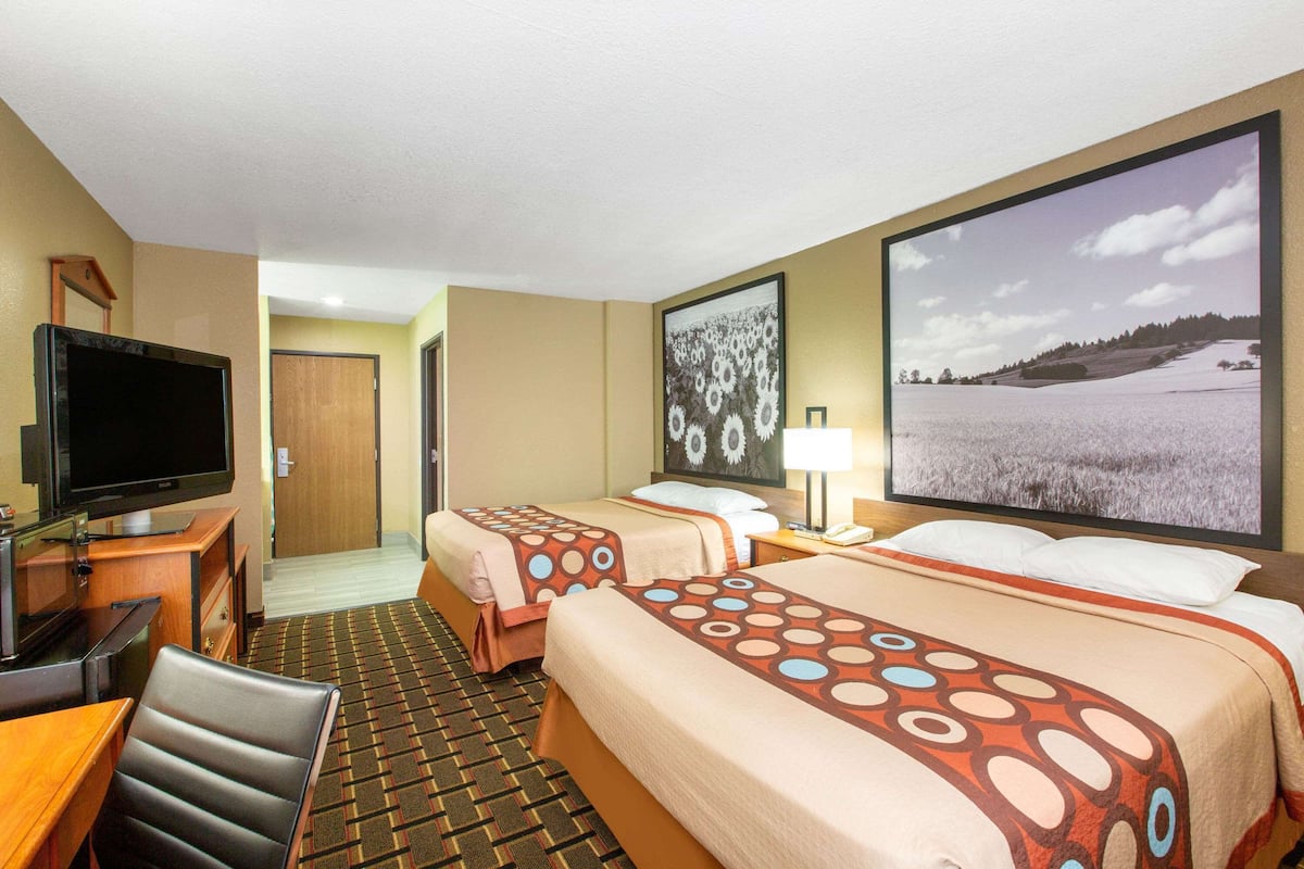 A hotel room with two beds, a TV, a desk, and a chair.