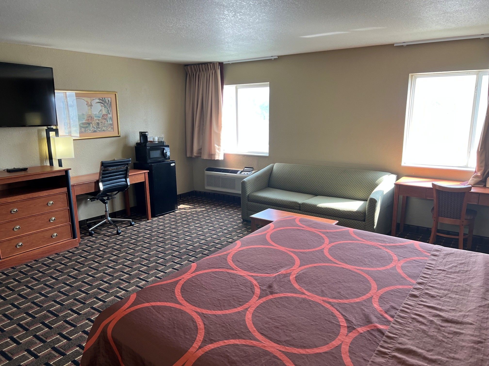 A hotel room with a bed, a desk, a chair, a television, and a window.