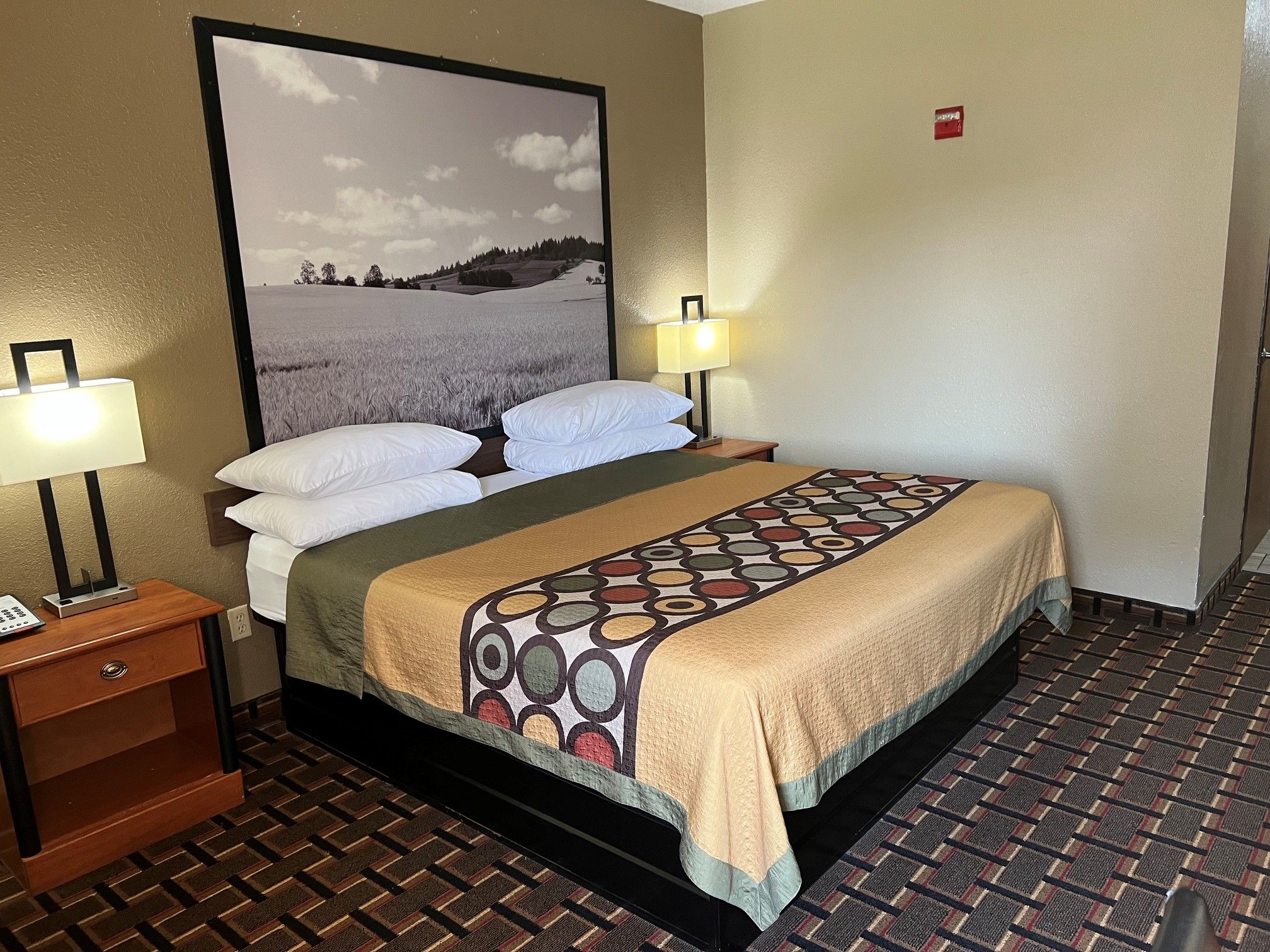 Een hotelkamer met een bed, twee bedlampen, een nachtkastje, een telefoon en een aan de muur hangend schilderij.