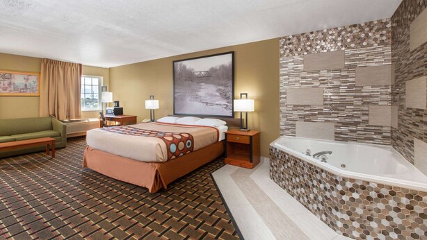 A hotel room with a large bed, a sitting area with a sofa and a table, a desk, a large window, and a bathroom with a bathtub and mosaic tiles. - Super 8 by Wyndham Ottawa (Ottawa)