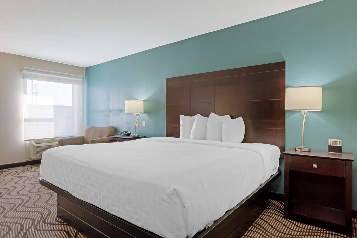 A hotel room with a large bed, two bedside tables with lamps, a chair, and a window with blinds.