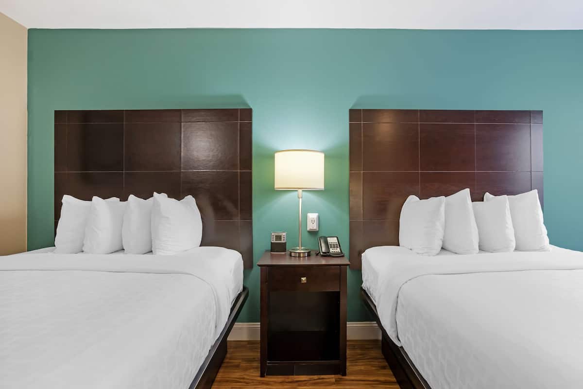 A hotel room with two beds, a nightstand with a lamp, a phone, and a small table.