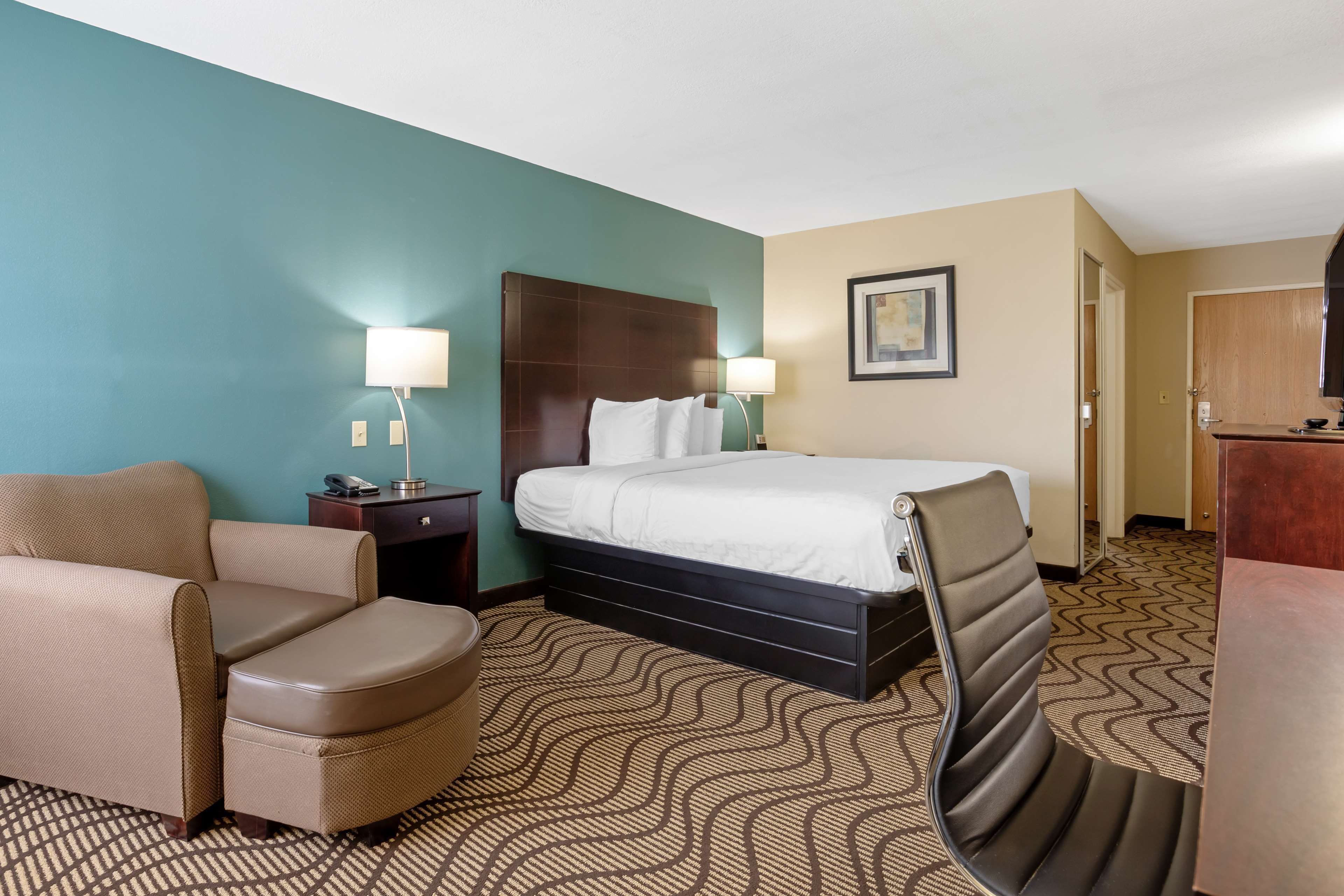 A hotel room with a bed, a chair, a desk, and a lamp.