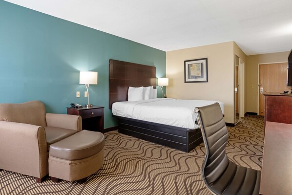A hotel room with a bed, a chair, a desk, and a lamp.